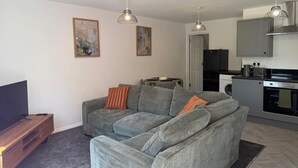 Een moderne woonkamer met een grijze bank, een flatscreen televisie en hanglampen.