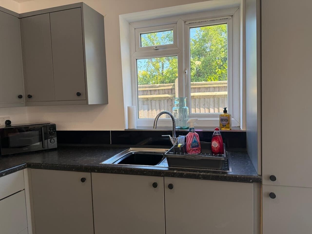 Una cocina con un lavamanos doble, un microondas, armarios y una ventana con vistas a árboles.