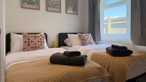 Een hotelkamer met twee bedden, beddengoed met een patroon, een raam met gordijnen, en drie ingelijste kunstwerken aan de muur.