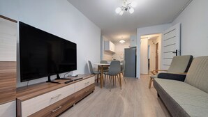 Un salon moderne doté d’un téléviseur à écran plat, de meubles en bois, d’un coin repas avec des chaises et d’un canapé.