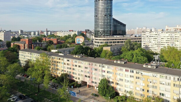 Un immeuble de grande hauteur à la façade incurvée, entouré d’immeubles résidentiels de taille moyenne et de verdure.