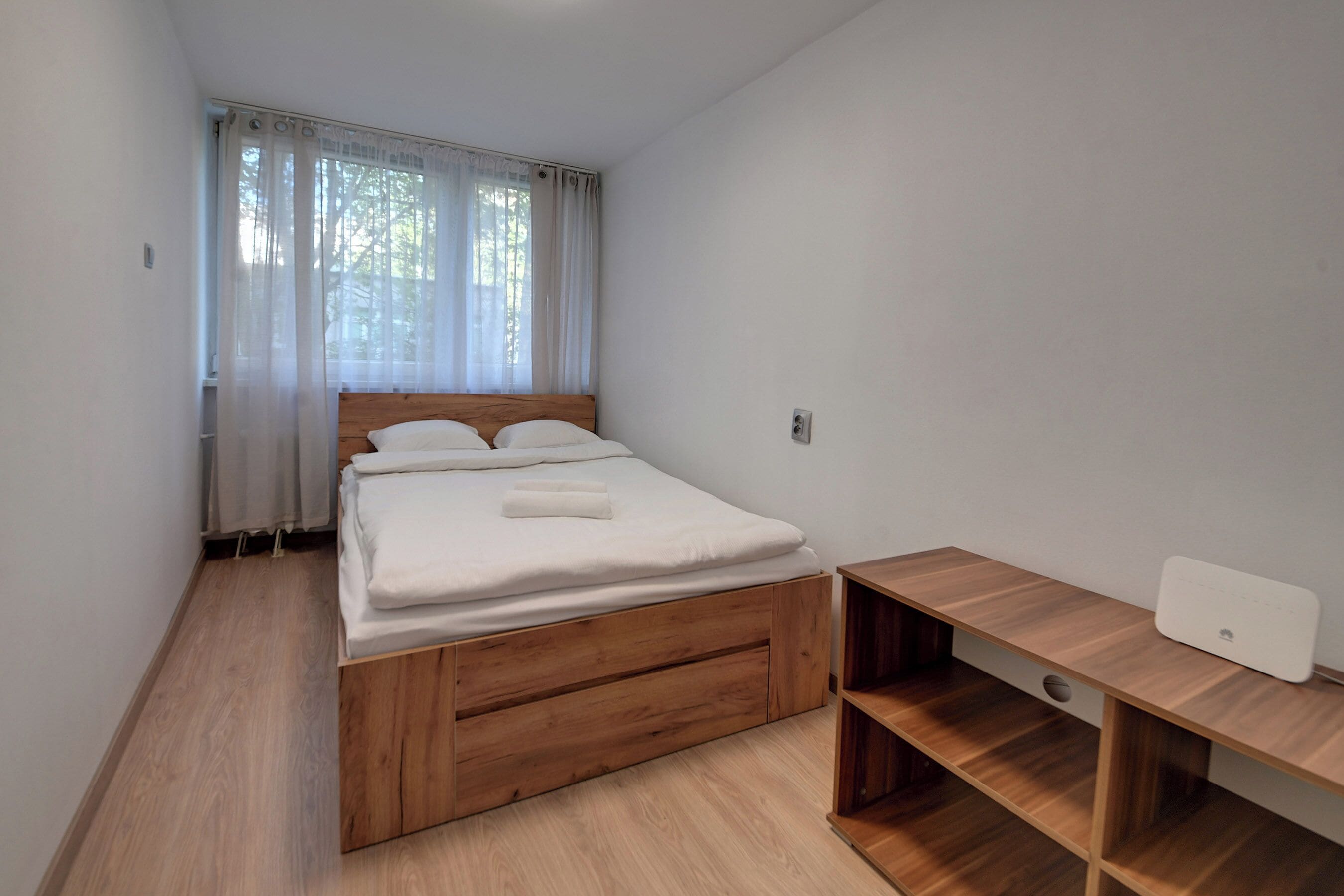 Ein Schlafzimmer mit einem hölzernen Bett, einem Schreibtisch und einem Fenster mit leichtem Vorhang.