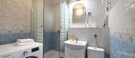 A modern bathroom with a built-in washer, a glass-enclosed shower, a sink, and a toilet.
