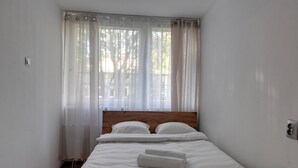 Un lit simple avec du linge de lit blanc, une tête de lit en bois et des rideaux en voile.
