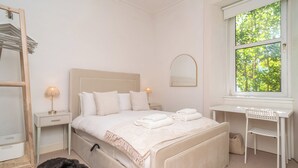 A bedroom with a bed, bedside tables, a desk, a chair, a window with a view, and a mirror. - Cosy 2 Bed in Central Edinburgh - Pass the Keys (Edinburgh)