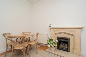Een kamer met een open haard, een eettafel met stoelen en een potplant.