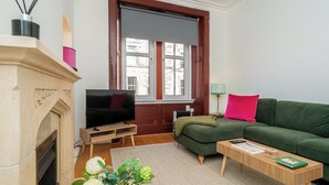 A living room with a fireplace, a television, a green sofa, a wooden coffee table, and a window with a view of buildings. - Cosy 2 Bed in Central Edinburgh - Pass the Keys (Edinburgh)