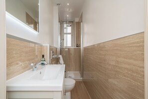 Een moderne badkamer met een wastafel, toilet en douchecabine met glazen wanden.