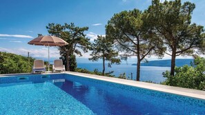 A swimming pool with two lounge chairs and an umbrella, surrounded by trees and a view of the sea. - Apartman Butterfly 2 - Opatija by Villas Guide (Brsec)