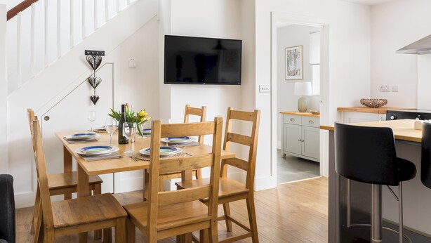 Una cocina moderna con comedor, sillas de madera, un televisor montado en la pared y una escalera que sube a otro nivel.