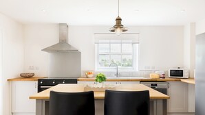 Una cocina moderna con una isla central, taburetes negros, una campana extractora de acero inoxidable y una ventana con vistas.