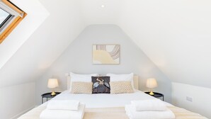 Un dormitorio con techo inclinado, una cama con ropa de cama blanca, dos lámparas de noche y una obra de arte colgada en la pared.