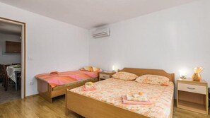 Ein Schlafzimmer mit zwei Einzelbetten, Holzboden, einem kleinen Nachttischchen mit Lampe und einer Klimaanlage an der Wand.