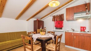 Ein Essbereich mit einem Tisch für vier Personen, Holzstühle, eine Holzbalkendecke, eine Küche mit Holzausstattung und ein Fenster mit roten Vorhängen.