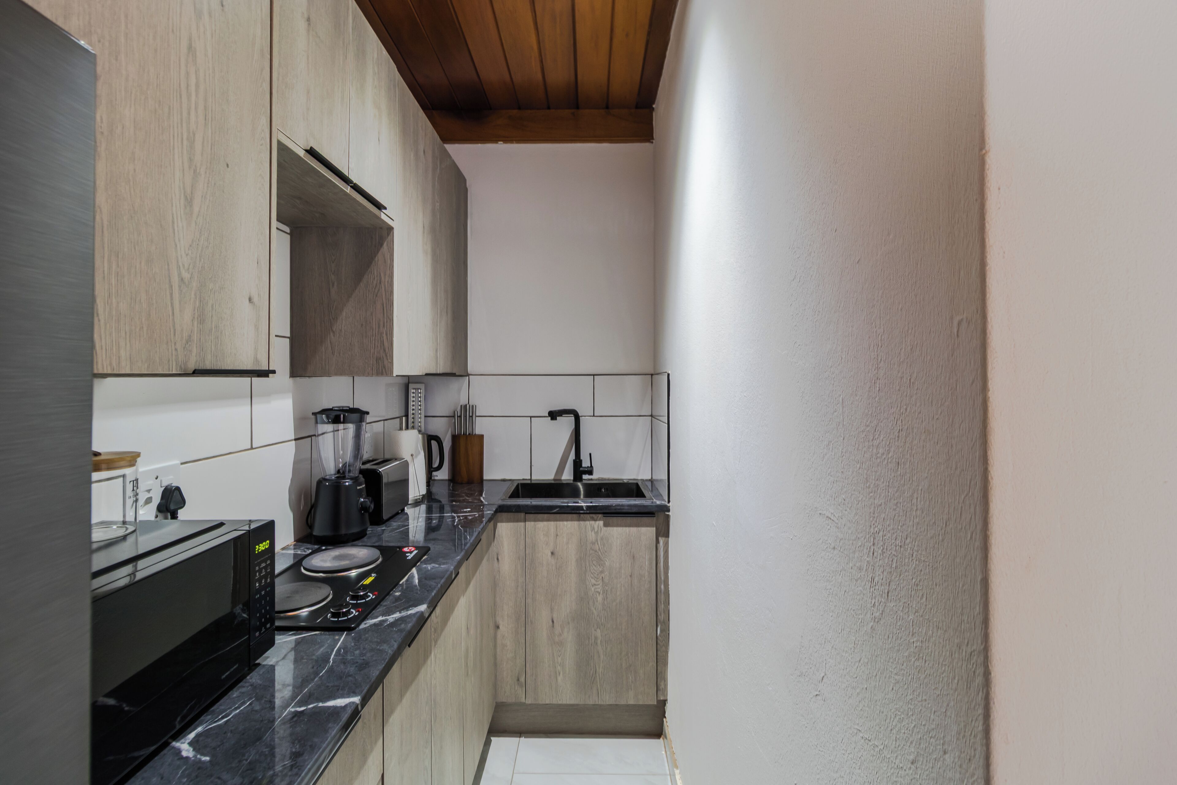 A narrow kitchen with a black countertop, a microwave, a blender, and a sink.