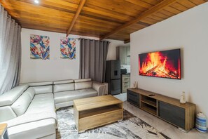 Ein Wohnzimmer mit einem Ecksofa, einem Holztisch, einem Fernseher und Kunstwerken an der Wand.