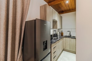 A modern kitchen with a stainless steel refrigerator, wooden cabinets, a built-in oven, and a black countertop. - Boutique Hotel-Style Room In Ferndale-F6 (Randburg)