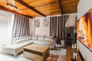 A modern living room with a sectional sofa, a wooden coffee table, a flat-screen TV, and a refrigerator. - Boutique Hotel-Style Room In Ferndale-F6 (Randburg)