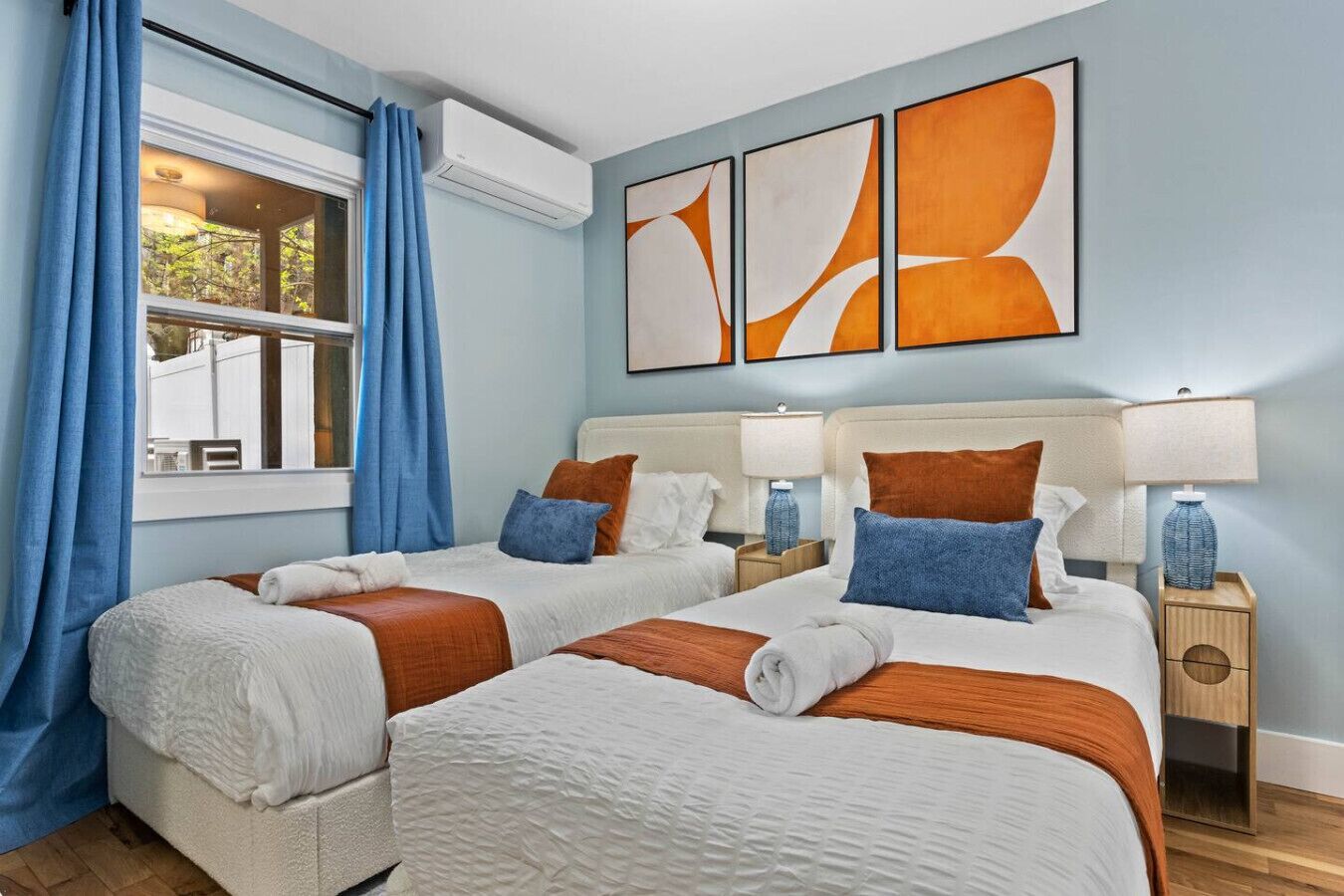 Een hotelkamer met twee bedden, een raam met gordijnen, een airconditioning en abstracte wanddecoratie.