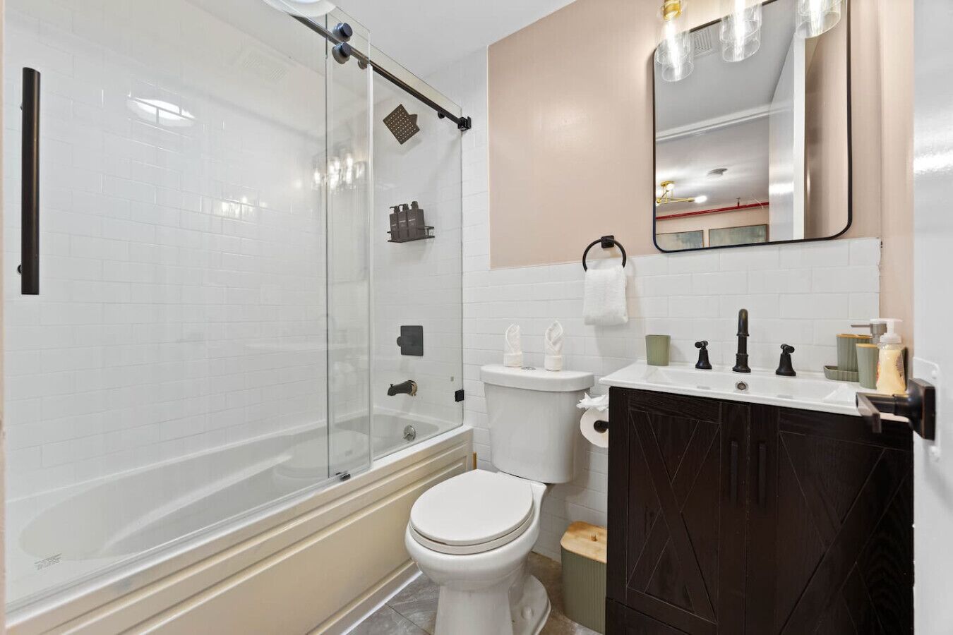 Un baño moderno con ducha envuelta en vidrio, inodoro blanco y tocador de madera oscura.