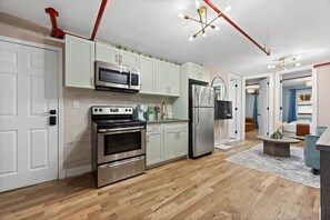 A modern kitchen with stainless steel appliances, light green cabinets, and a wooden floor.