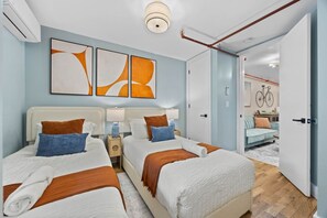 A hotel room with two beds, a large abstract painting, a bicycle in the background, and a wooden floor. - Only in Brooklyn | 2BR + Backyard • Full Kitchen (Brooklyn)