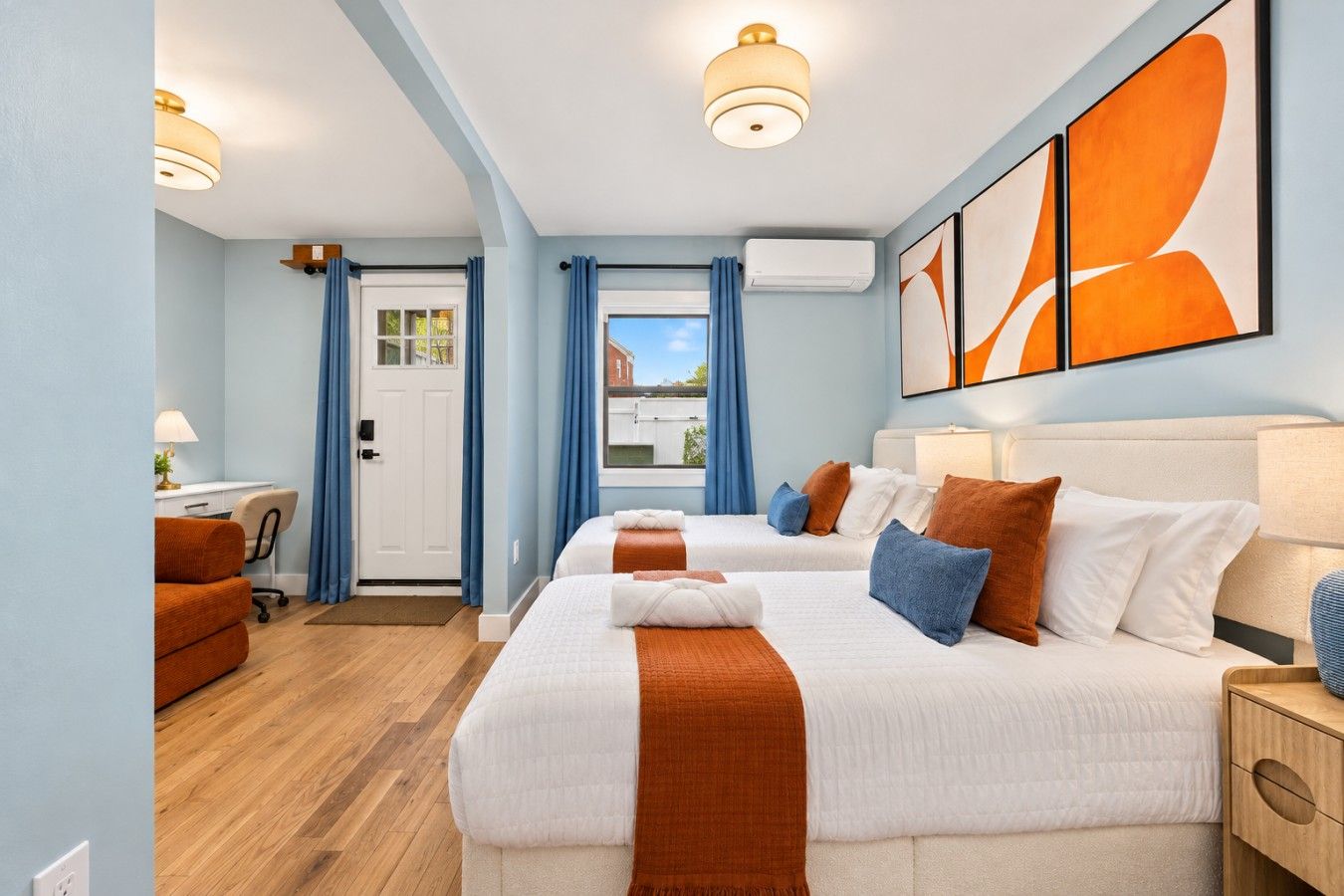 A hotel room with two beds, a desk, a chair, and a view of the outside.
