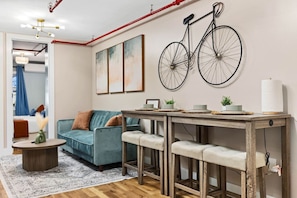 Ein Wohnzimmer mit einer Couch, einem Couchtisch, einem Esstisch mit Hocker sowie einem an der Wand befestigten Fahrrad und abstrakter Kunst.