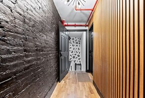 Ein schmaler Flur mit einer Backsteinwand an einer Seite, einer Holzwand an der anderen und einer verzierten Tür am Ende.