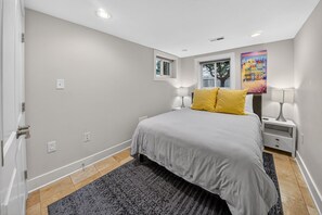 Une chambre à coucher avec un lit, deux tables de chevet, une fenêtre et un tableau au mur.