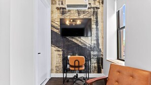 Ein Zimmer mit einem wandmontierten Flachbildfernseher, einem Schreibtischstuhl, einem Fenster mit Blick und einer Wand mit einem strukturierten Wandgemälde.