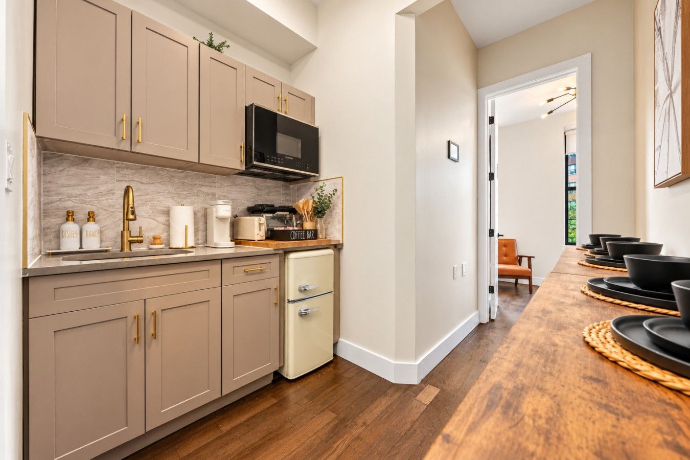 A kitchen with beige cabinets, a microwave, a coffee maker, and a coffee bar sign.