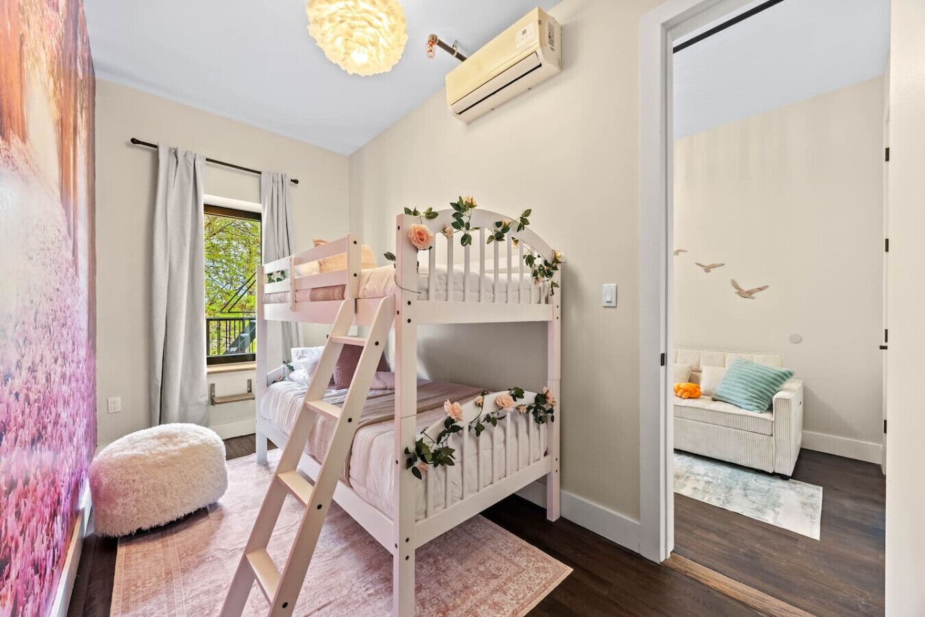 Uma cama beliche para criança, uma escada, um sofá branco, uma janela com cortinas e um aparelho de ar condicionado.