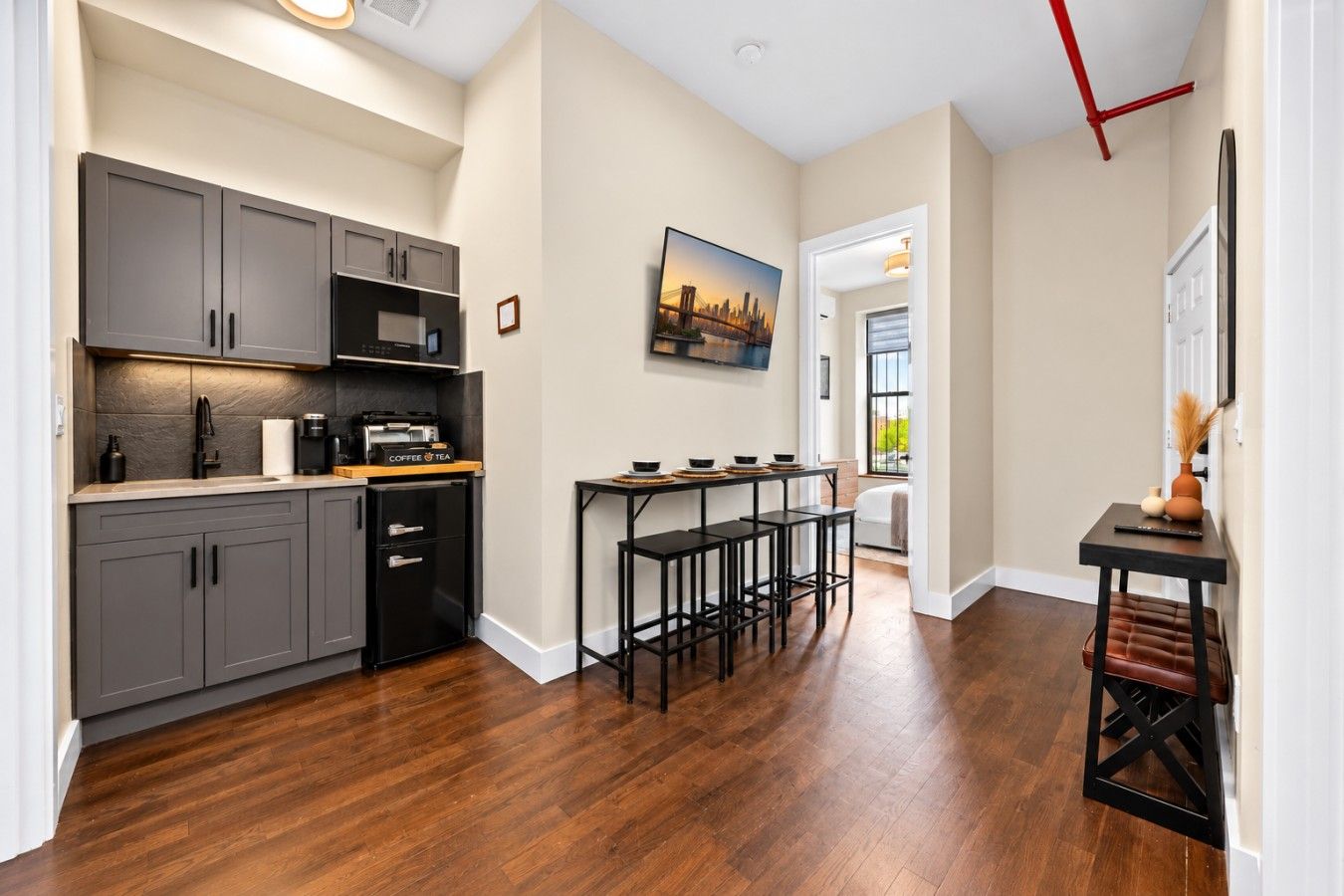 A modern kitchen with grey cabinets, a coffee machine, and a dining area with stools.