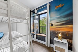 Camera con letto a castello, un'ampia finestra, un comodino e un murale raffigurante un aereo.