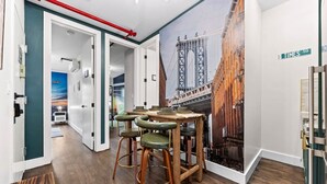 Ein Gang mit Wandgemälde einer Brücke, einem Holztisch mit Hockern und einem Schild mit dem Schriftzug Times Square.
