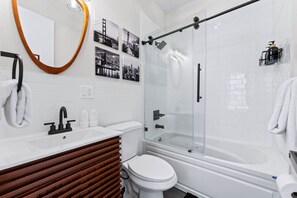 Un baño moderno con cabina de ducha de vidrio, inodoro blanco, tocador con espejo y perchero.