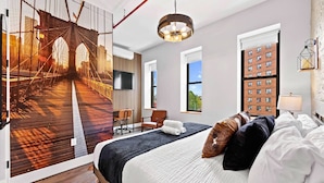 Ein modernes Hotelzimmer mit einem großen Bett, einem Schreibtisch, einem Sessel und Blick auf die Stadt durch das Fenster.