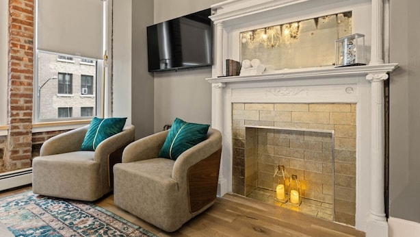 A living room with a fireplace, two armchairs, a television mounted on the wall, and a patterned rug.