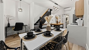 A modern dining area with a white table, black chairs, and a staircase in the background.