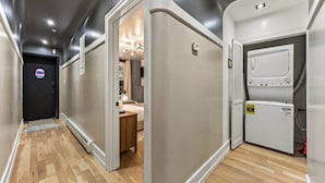A hallway with a wooden floor, a black door with a circular window, and a room with a bed and a desk.
