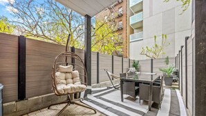 A patio area with a wicker chair, a glass table, and a striped rug.