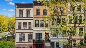 Une rangée d’immeubles à plusieurs étages, dotés d’une échelle de secours, d’une devanture de magasin bien visible et d’un arbre au premier plan.