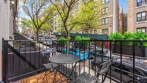 A balcony with a table and chairs, a view of parked cars, and buildings in the background. - Romantic Manhattan Micro-Suite + Private Balcony (New York)