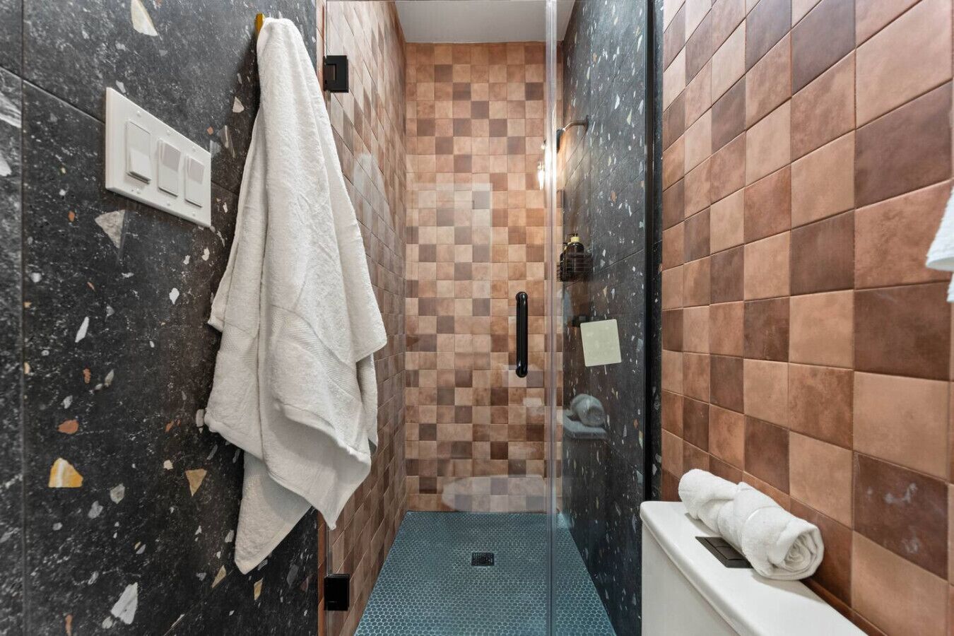 Een badkamer met een geruite vloer, een douchecabine van glas en een handdoekrek.