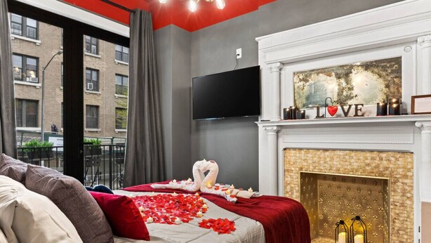 A hotel room with a bed, a fireplace, a TV, and a balcony view. - Romantic Manhattan Micro-Suite + Private Balcony (New York)