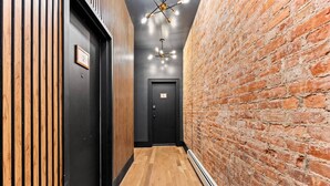 A hallway with wooden flooring, a brick wall, and black doors. - Romantic Manhattan Micro-Suite + Private Balcony (New York)