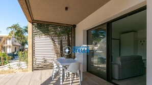 Eine moderne Terrasse mit Tisch und Stühlen, eine Glastür, die zu einem Wohnbereich führt, und ein Holzzaun.