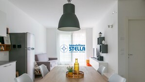 Un espace repas moderne avec une table en bois, des chaises blanches, un luminaire suspendu et un plateau décoratif contenant une bouteille et des fleurs.