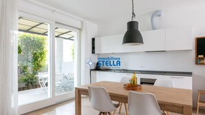 Une cuisine moderne avec des meubles blancs, une table à manger en bois et un luminaire suspendu noir.
